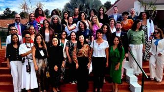 A group of mostly women standing on red steps in a location that looks warm and Brazilian. 