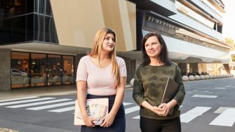 Two female mature age students walking together behind law building