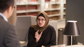 Student wearing hijab in law library, talking to tutor