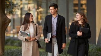 Three Law students walking in front of Law Building, dressed in smart attire, walking towards the camera, greenary and reflections in glass of law building in the background