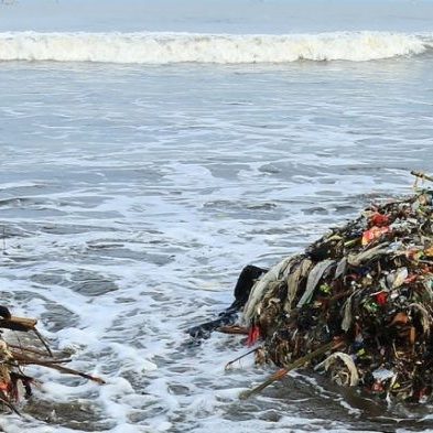 Piles of plastic waste and debris on a beach as ocean waves wash ashore.