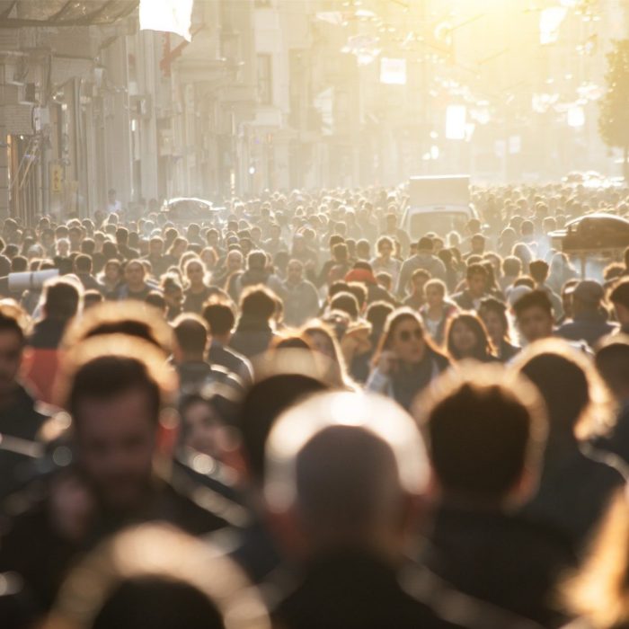 A large crowd of people walking down a sunlit city street.