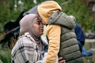 Rear view of unrecognizable children of different ages holding hands while coming in to migrant camp