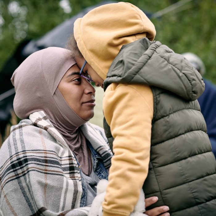 Happy middle-eastern mother in headscarf touching foreheads with daughter while finding her after escape from battlefield
