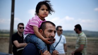 Idomeni, Greece - May 26, 2016. A Syrian man carries his daughter, as refugees abandon the makeshift camp of Idomeni in northern Greece, after the evacuation operation by the Greek police.