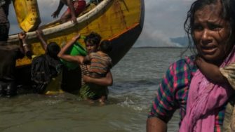 a woman holding her baby and a boat behind her in the water