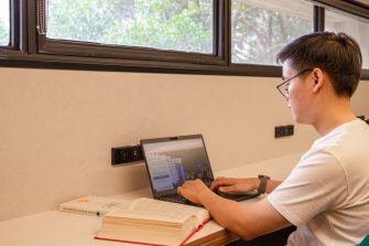 A student sitting in front of the south windows, using their laptop.