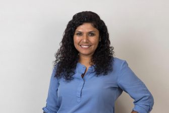 A smiling woman with curly hair wearing a blue blouse, posing against a plain background. This image is suitable for professional and academic purposes.