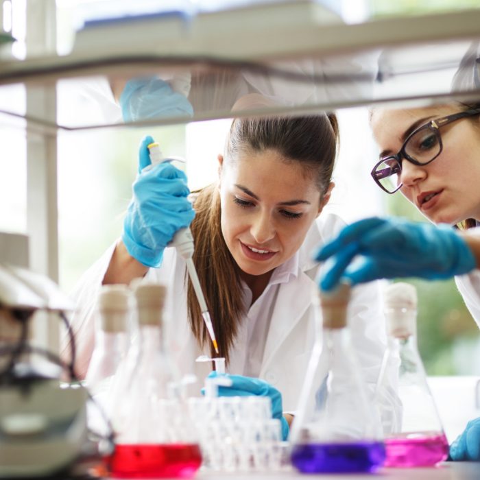 Two dedicated female lab scientists meticulously work together, focusing on chemical research and experiments, advancing scientific knowledge.
