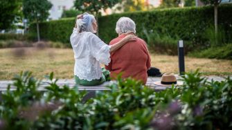 Elderly mother sitting on bench with adult daughter, spending sunday together.