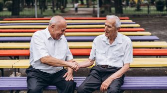 Two old senior adult men have a conversation outdoors in the city park