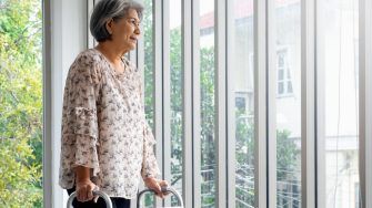 Senior woman standing with walking frame looking out the window