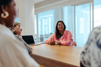 A female business owner is leading a meeting in a modern office environment. She is surrounded by diverse colleagues, all engaged in a discussion about new business strategies and ideas.