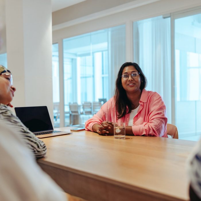 A female business owner is leading a meeting in a modern office environment. She is surrounded by diverse colleagues, all engaged in a discussion about new business strategies and ideas.