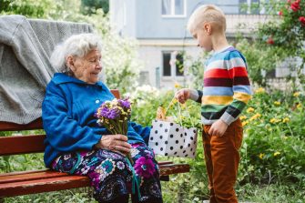 90 year old great-grandmother, grandmother with grandson together. Grandson hugs his beloved grandmother. Kid grandson came to grandmother with flower bouquet and food basket.