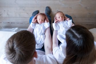 Newborn Identical twins on the bed, on a parents hands. Life style, emotions of kids. Infant Babies With Copy. Space
