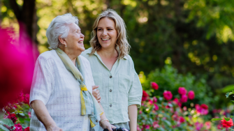 An adult granddaughter supporting her senior grandmother when taking her for a walk in the park.