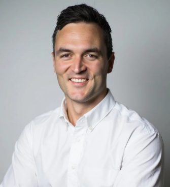 A man in a white business shirt is looking into the camera smiling
