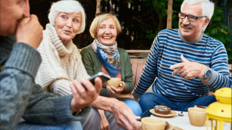 Four elderly people having tea outside and engaging in fun conversation