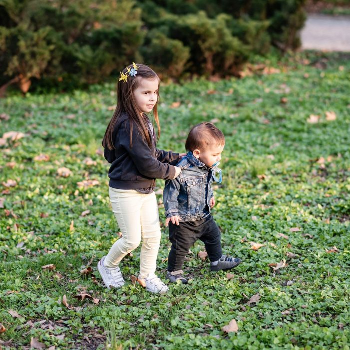 Older sister helping younger brother learning to walk in park
