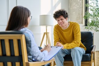Happy teenage boy smiling during successful consultation with female psychologist or career counselor. Positive mental health progress, psychotherapy counseling, youth therapy or educational guidance