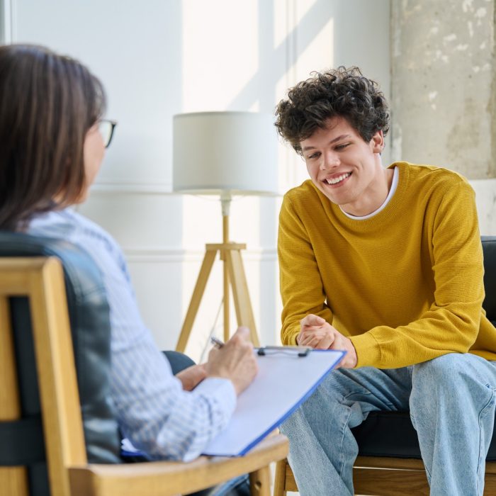 Happy teenage boy smiling during successful consultation with female psychologist or career counselor. Positive mental health progress, psychotherapy counseling, youth therapy or educational guidance