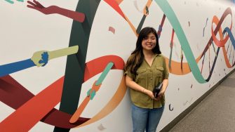 Student Helen Han standing in front of "Embracing Diversity" mural in the Wallace Wurth building