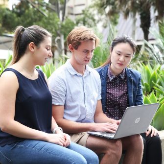 Three students sitting on a wall, working