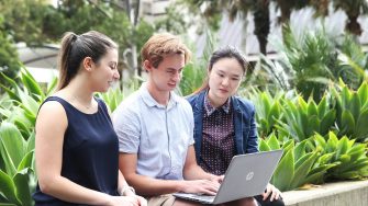 Three students sitting on a wall, working