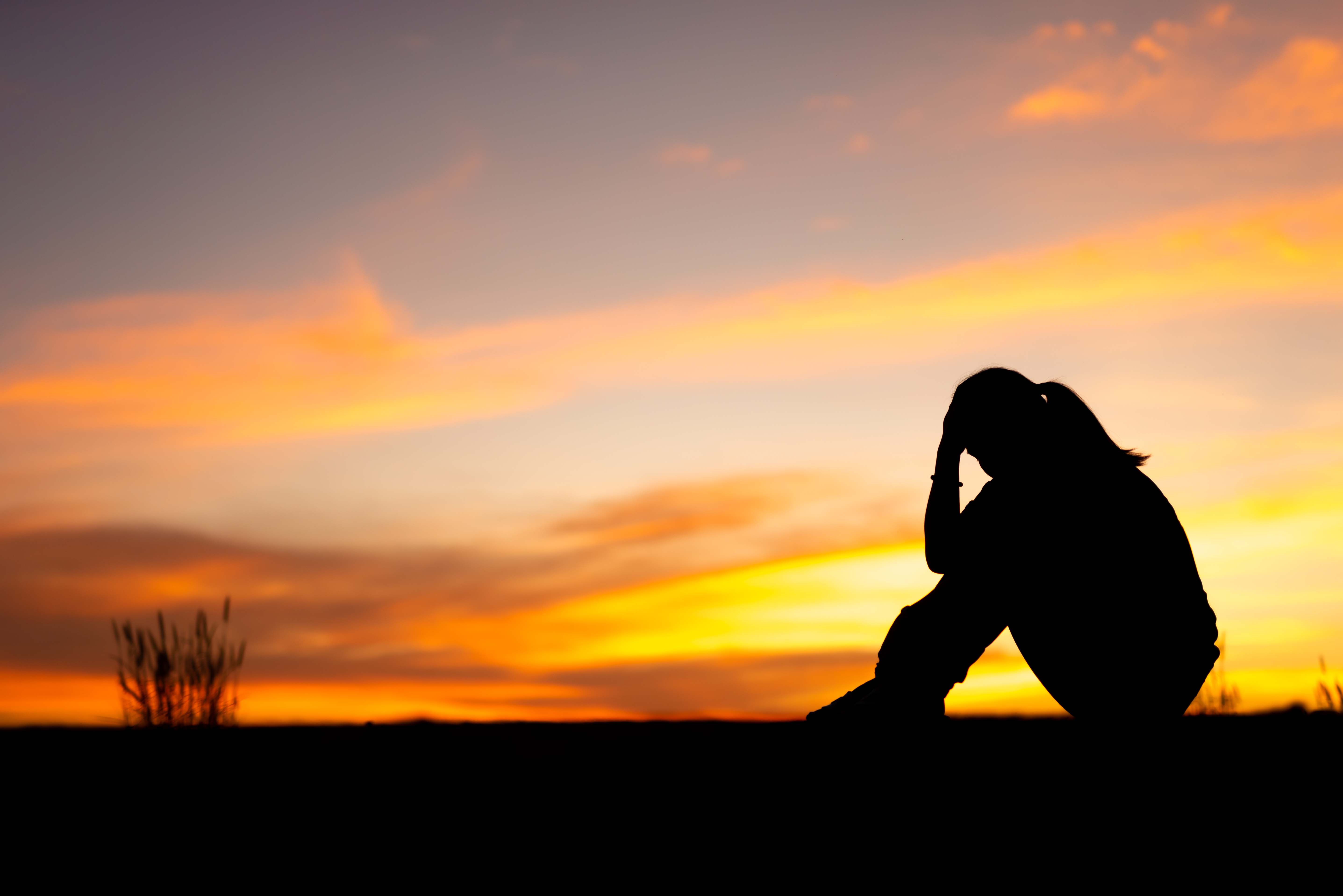 Silhouette of sad woman sitting in park with sunset