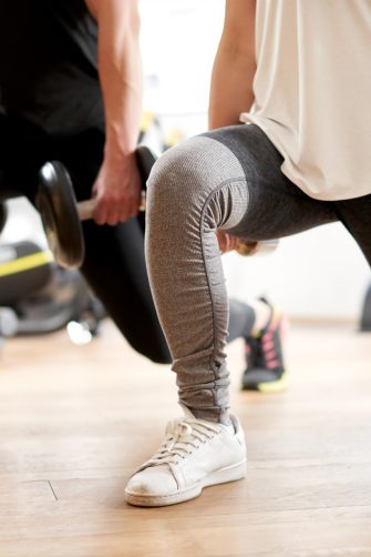 Two people do lunges at a gym while holding hand weights