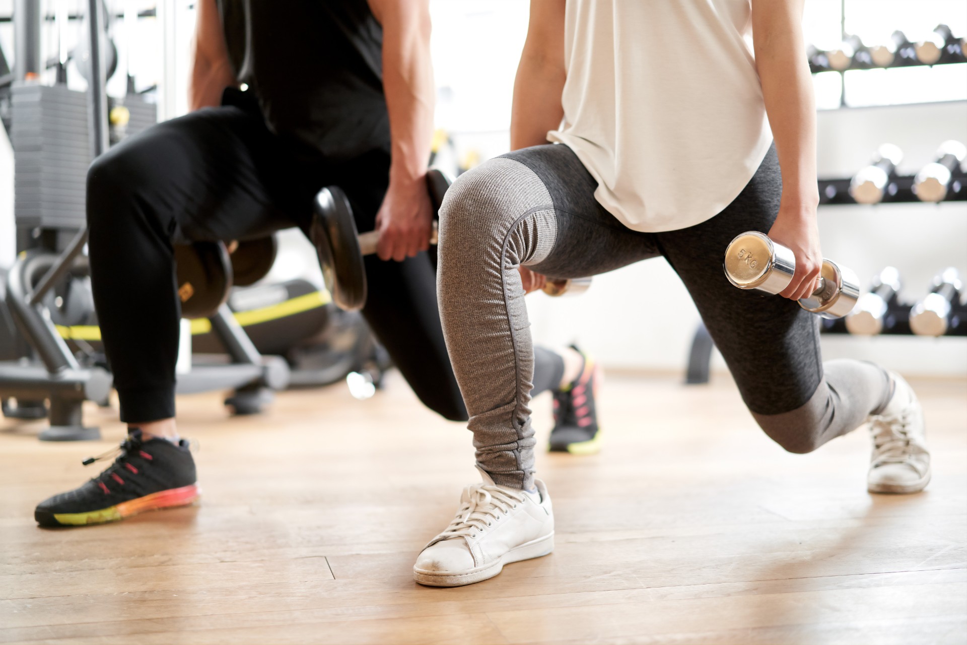 Two people do lunges at a gym while holding hand weights