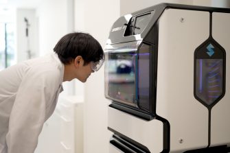  a man wearing a white uniform looking at  3d printer