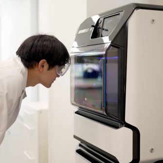  a man wearing a white uniform looking at  3d printer