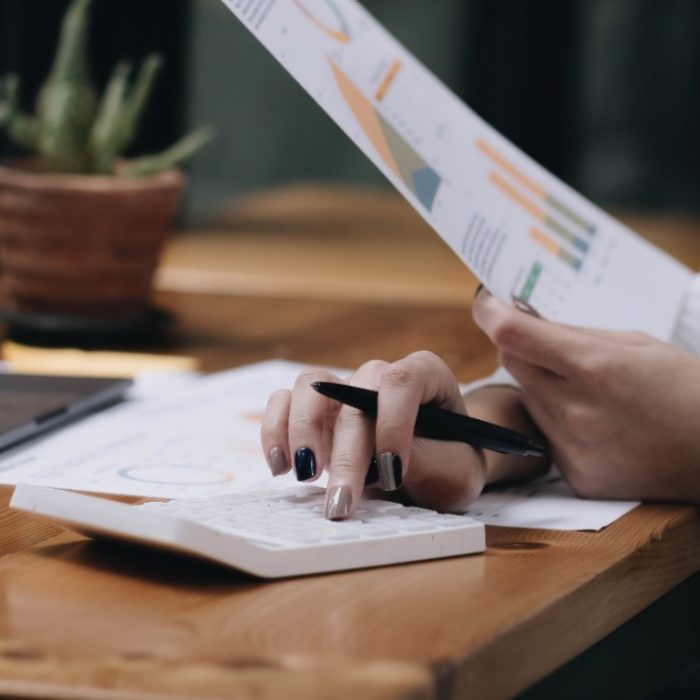 Close-up woman hand press calculator to calculate the company's financial results On the wooden table in the office and business work background, tax, accounting, statistics, and analytical research.