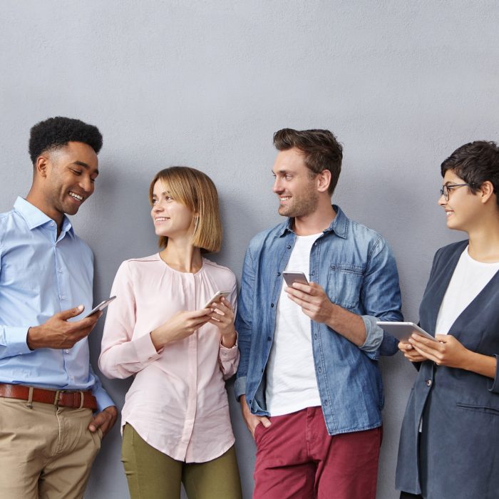 Portrait of colleagues being glad for their dark-skinned friend who is promoted at work, share happiness together, have pleasant smiles. Fashionable students meet at university after holidays