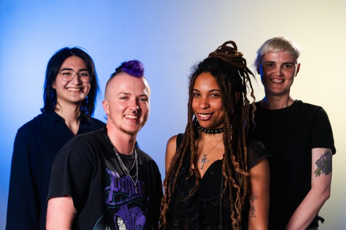 Four people posing for the camera against a blue and yellow background.
