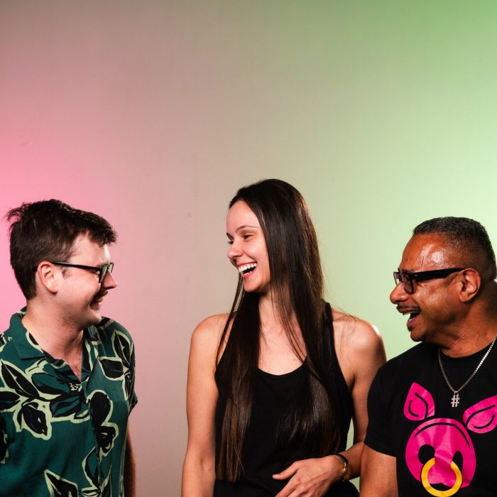 Three people are laughing together, looking towards the first person in the frame.