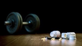 Steroid pills and capsules with dumbbell weight in the background - doping in sport