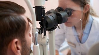 side view portrait of female ophthalmologist is looking through the slit lamp while examining eyesight of man patient in clinic