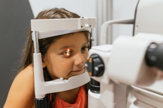 Optometrist conducting an eye exam on a young girl using a phoropter in a modern clinic, focusing on vision health and care