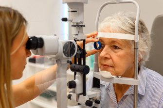 Female ophthalmologist using diagnostic lens during slit lamp test to examine senior woman's eyes at clinic