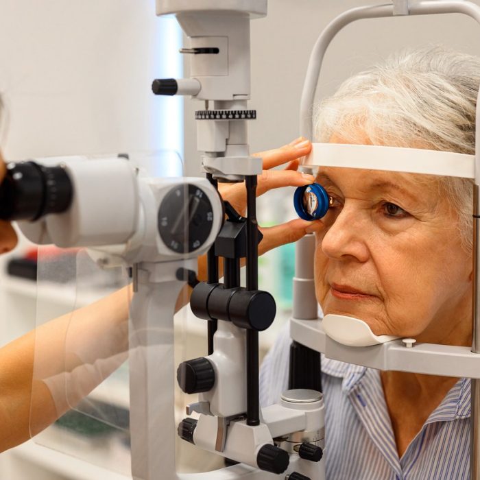 Female ophthalmologist using diagnostic lens during slit lamp test to examine senior woman's eyes at clinic