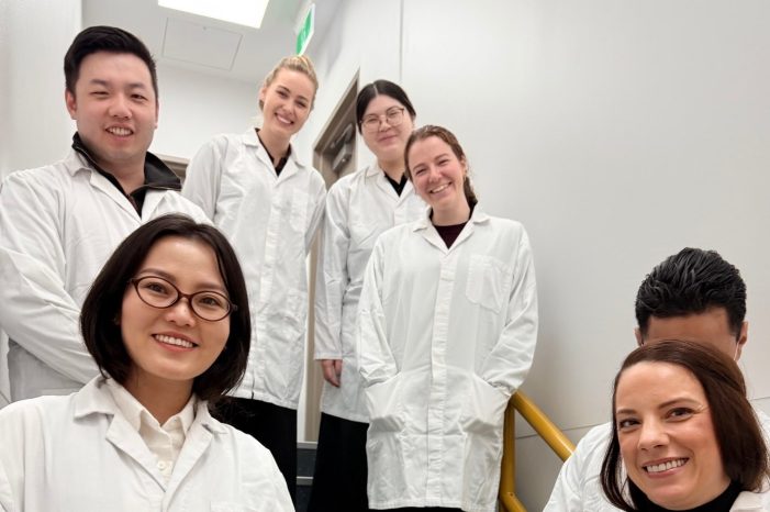 SPH MHLM students on a tour of Liverpool hospital pose for a photo on stairs, wearing protective gown and shoe covers