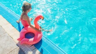 child sitting on edge of pool with flamingo blow up floaty