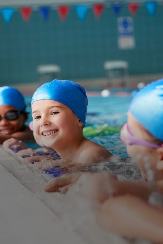 Portrait Of Children In Water At Edge Of Pool Waiting For Swimming Lesson