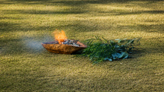 Elements of an Aboriginal smoking ceremony - a bark enclosed fire and branches, sit on a grassed area