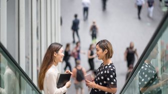 Two women smile and chat on an escalator in Sydney's CBD