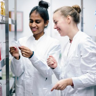 Two science students in lab coats happily look at the results on a petrie dish 