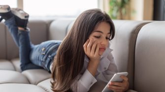 Digital Depression. Unhappy Preteen Girl Using Smartphone Reading Depressing News And Suffering From Lack Of Communication Lying On Sofa At Home. Gadgets Technology And Negative Emotions